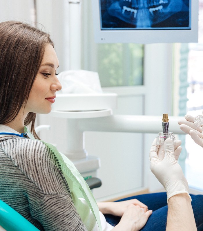 Dentist showing sample oversized implant to patient