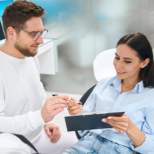 Man in white handing woman in dental chair forms on clipboard