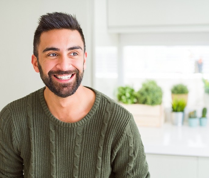 Man with brown hair in olive green sweater smiling in white kitchen