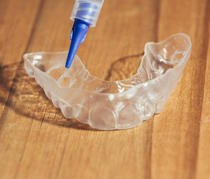 Applicator placing bleaching gel into a teeth whitening tray