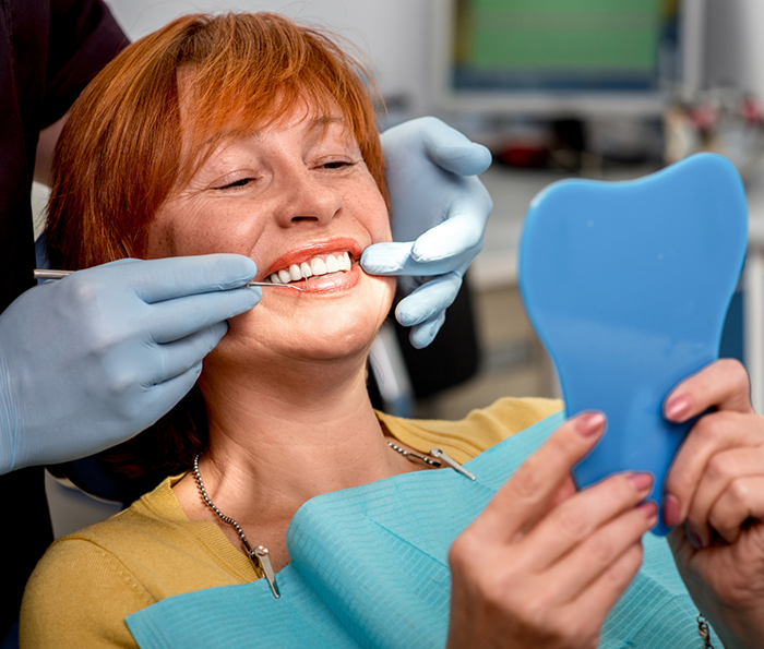 Woman in dental chair looking at her smile in a mirror