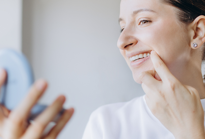 Woman looking at reflection of her smile with dental bridges in Salmon Creek