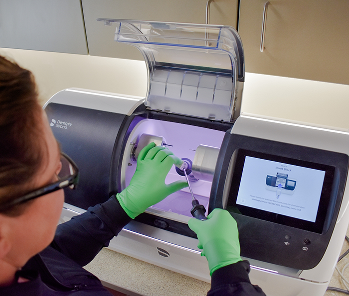Dentist placing a ceramic block into a machine for same day dental crowns