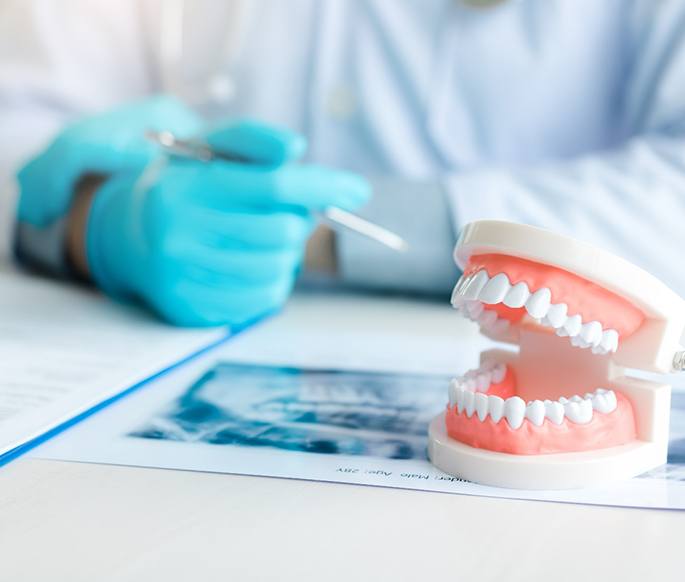 Dentist’s hand at desk with model teeth and X-rays