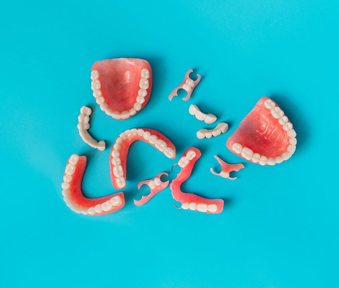 Bird’s eye view of several sets of full and partial dentures and bridegs on light blue surface