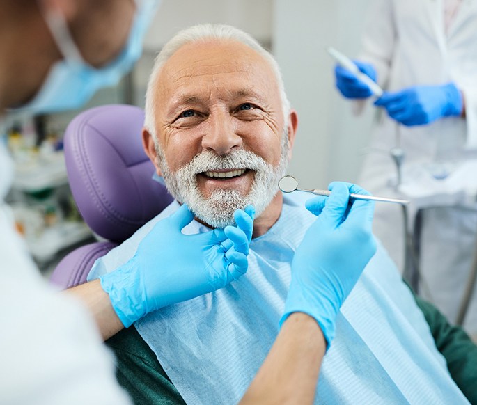 Gloved hands touching man’s chin about to examine his teeth