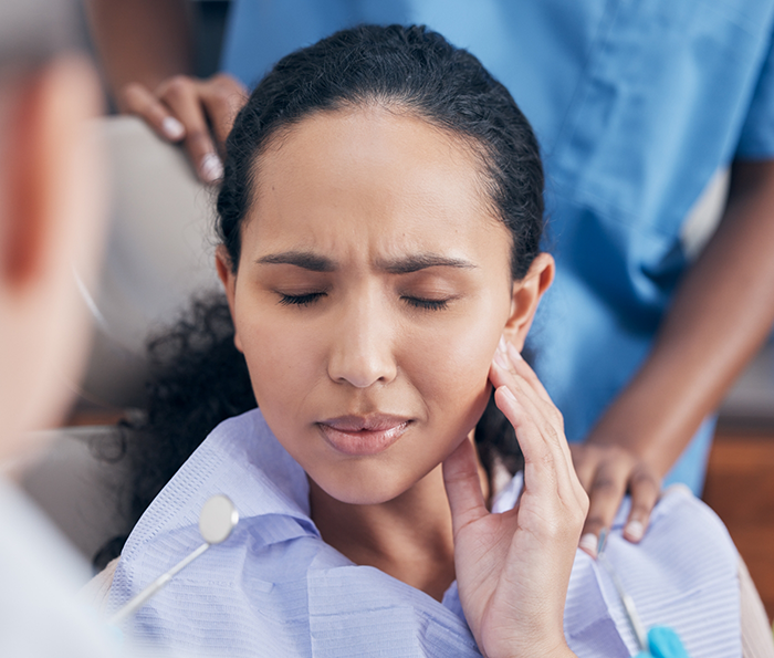 Dental patient wincing and holding her cheek in pain