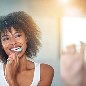 Woman with curly hair smiling as she brushes her teeth