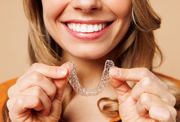 Smiling woman holding a Sure Smile clear aligner in Salmon Creek