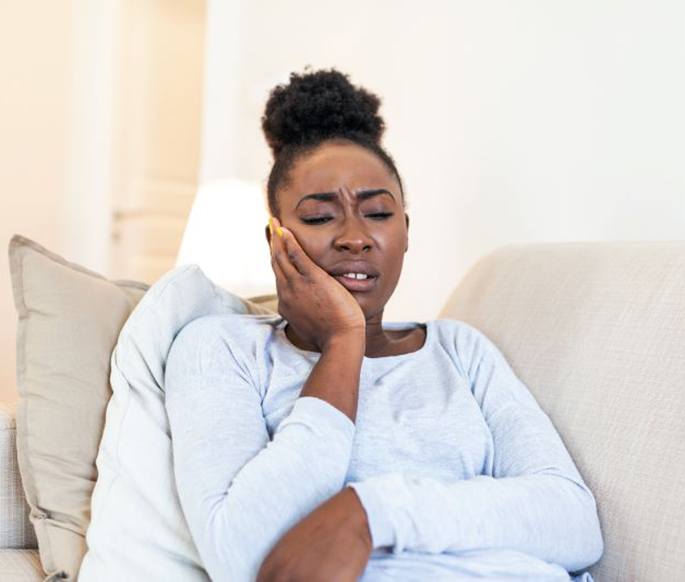 Woman sitting on sofa, struggling with dental implant pain