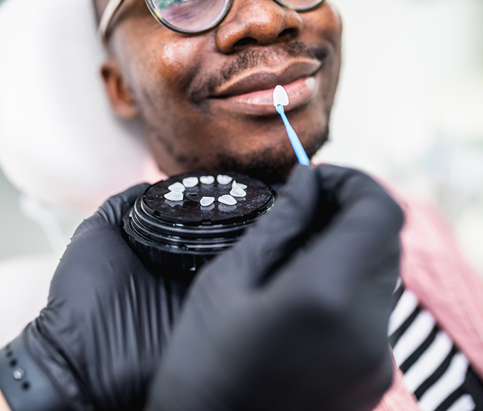 Dentist holding a veneer to a patients smile