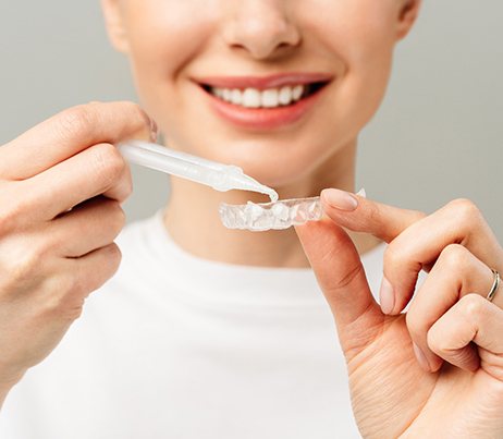 Nose-to-chest view of woman applying whitening gel to custom-fitted tray