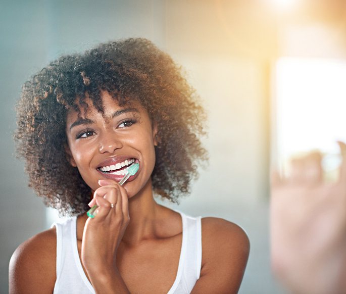 Woman brushing teeth in front of bathroom mirror
