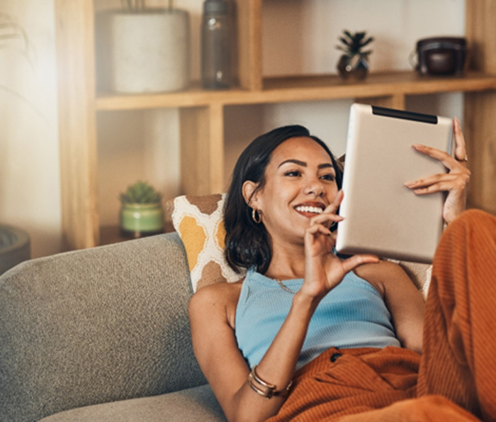 Smiling woman looking at tablet while relaxing on couch