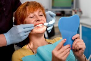 Woman with implants smiling into mirror in dentist's chair. 