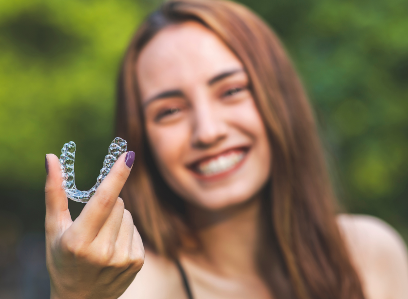 Woman holding clear aligner up to camera